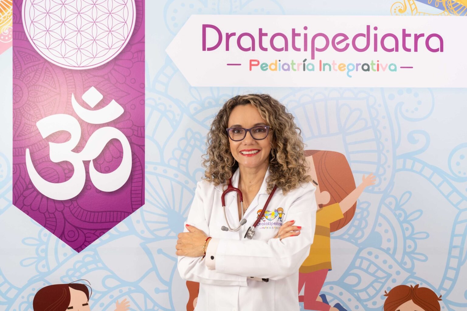 Pediatra posando cruzada de brazos frente a letraro de pediatra integrativa